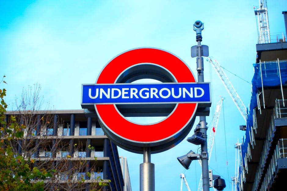 A station signage board at Ealing Broadway tube station displaying directions for the district line, Elizabeth line, and national rail buses, positioned on a paved platform with a shadow cast on the g